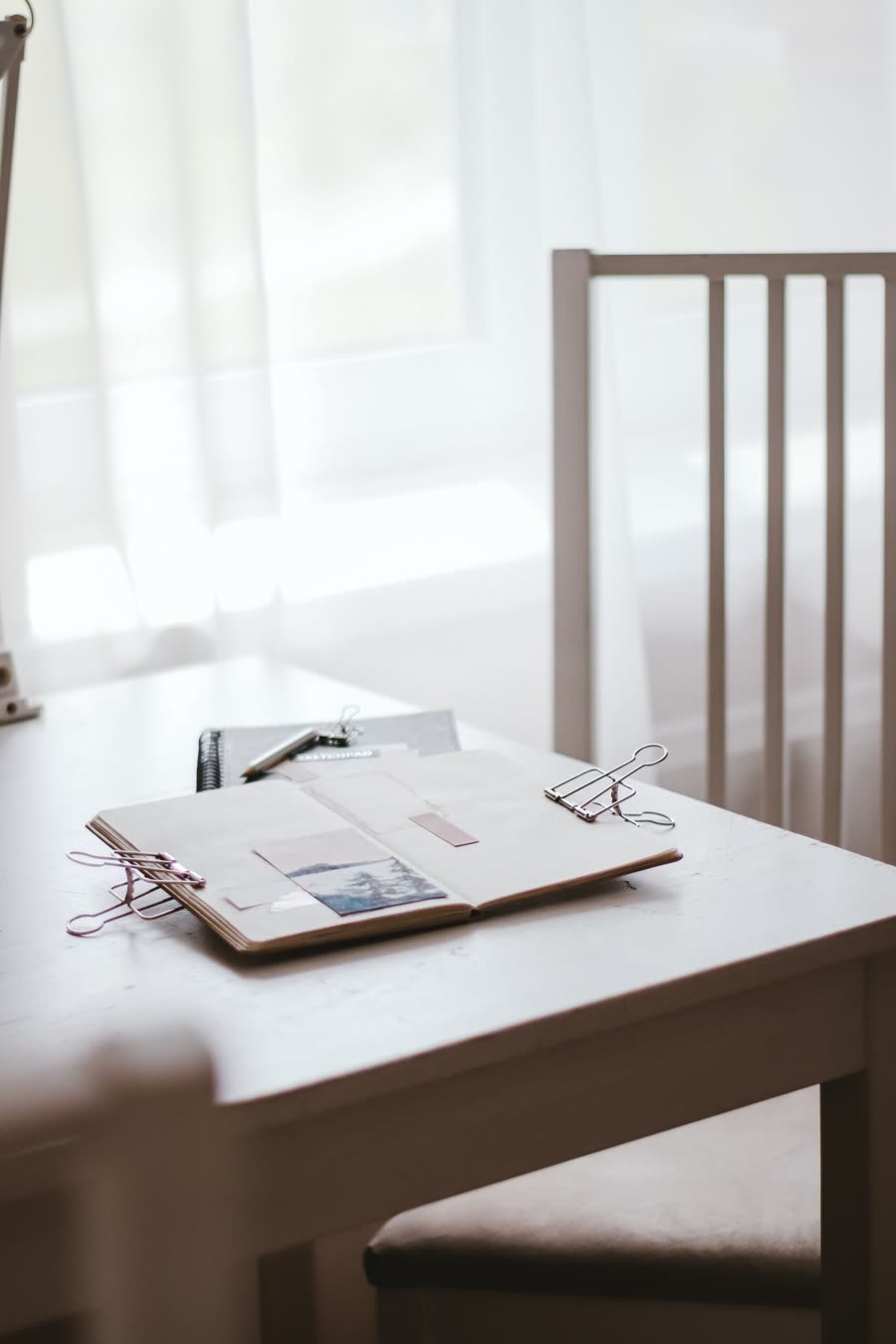 An open notebook with binder clips on a white desk by a sunlit window